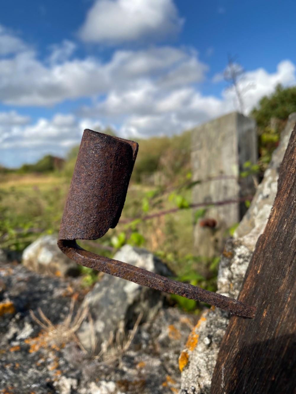 A primitive hand-forged wrought iron candle socket mounted on a pointed spike inserted into a thick piece of weathered timber. View VI