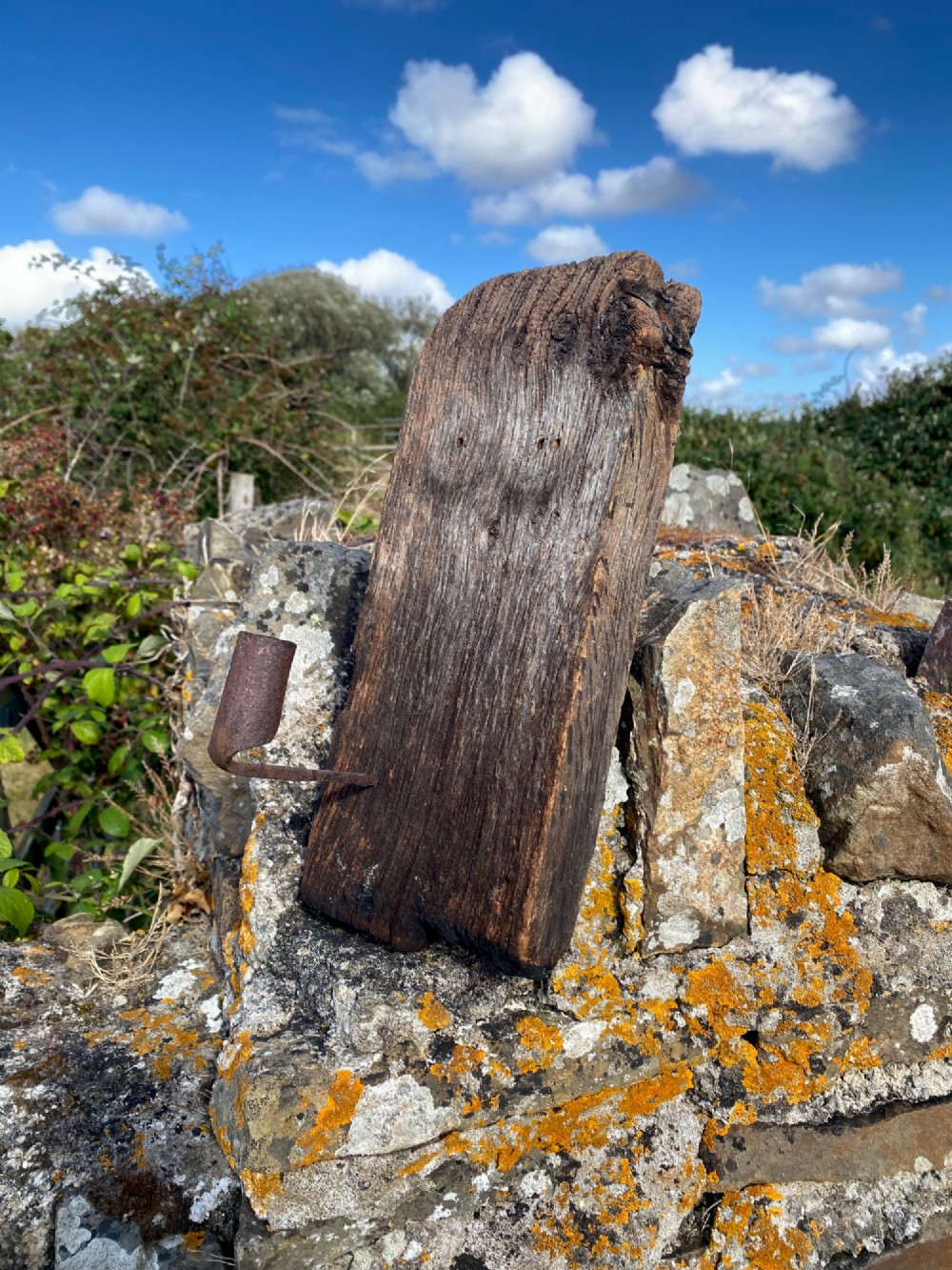 A primitive hand-forged wrought iron candle socket mounted on a pointed spike inserted into a thick piece of weathered timber. View VII