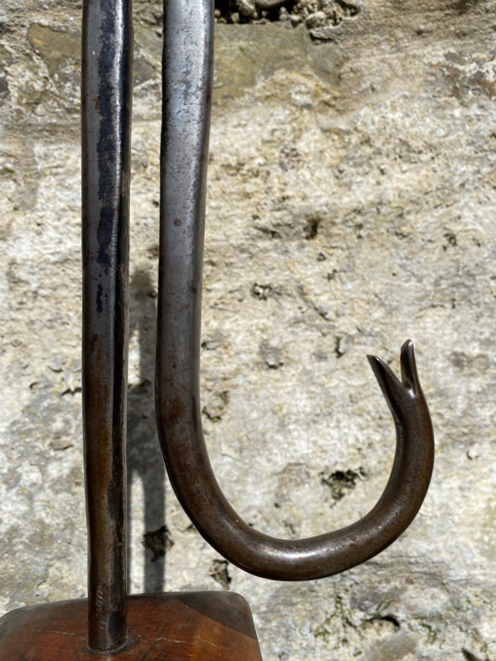 A forged steel tool with an integral lower hook mounted vertically into a square dark wooden block engraved with a cross and text. View IV