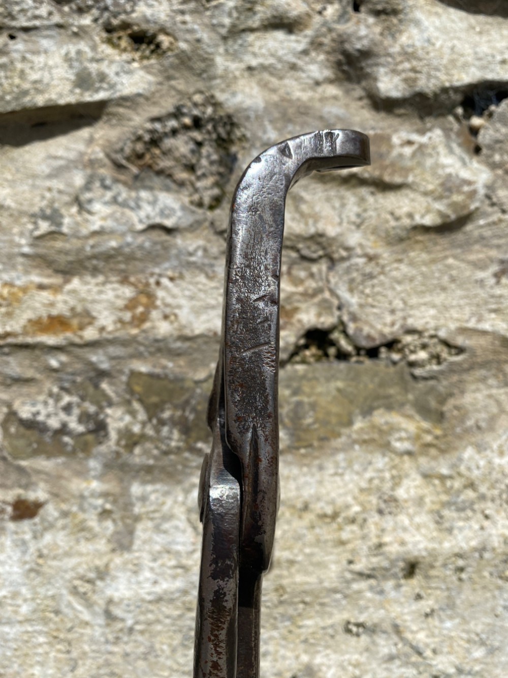 A forged steel tool with an integral lower hook mounted vertically into a square dark wooden block engraved with a cross and text. View VII