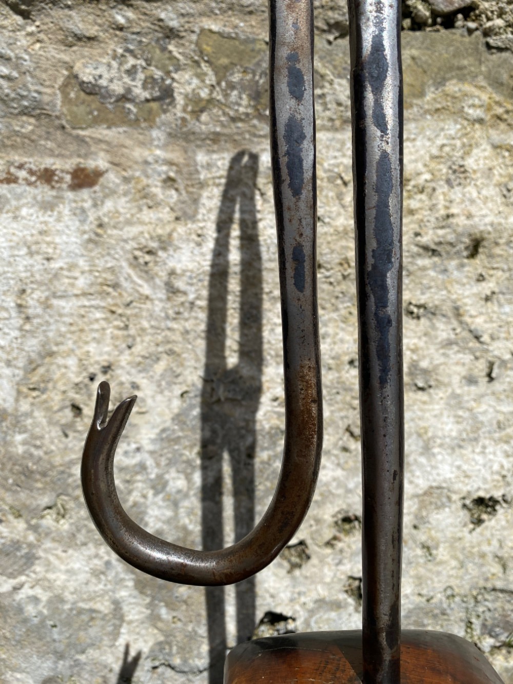 A forged steel tool with an integral lower hook mounted vertically into a square dark wooden block engraved with a cross and text. View IX