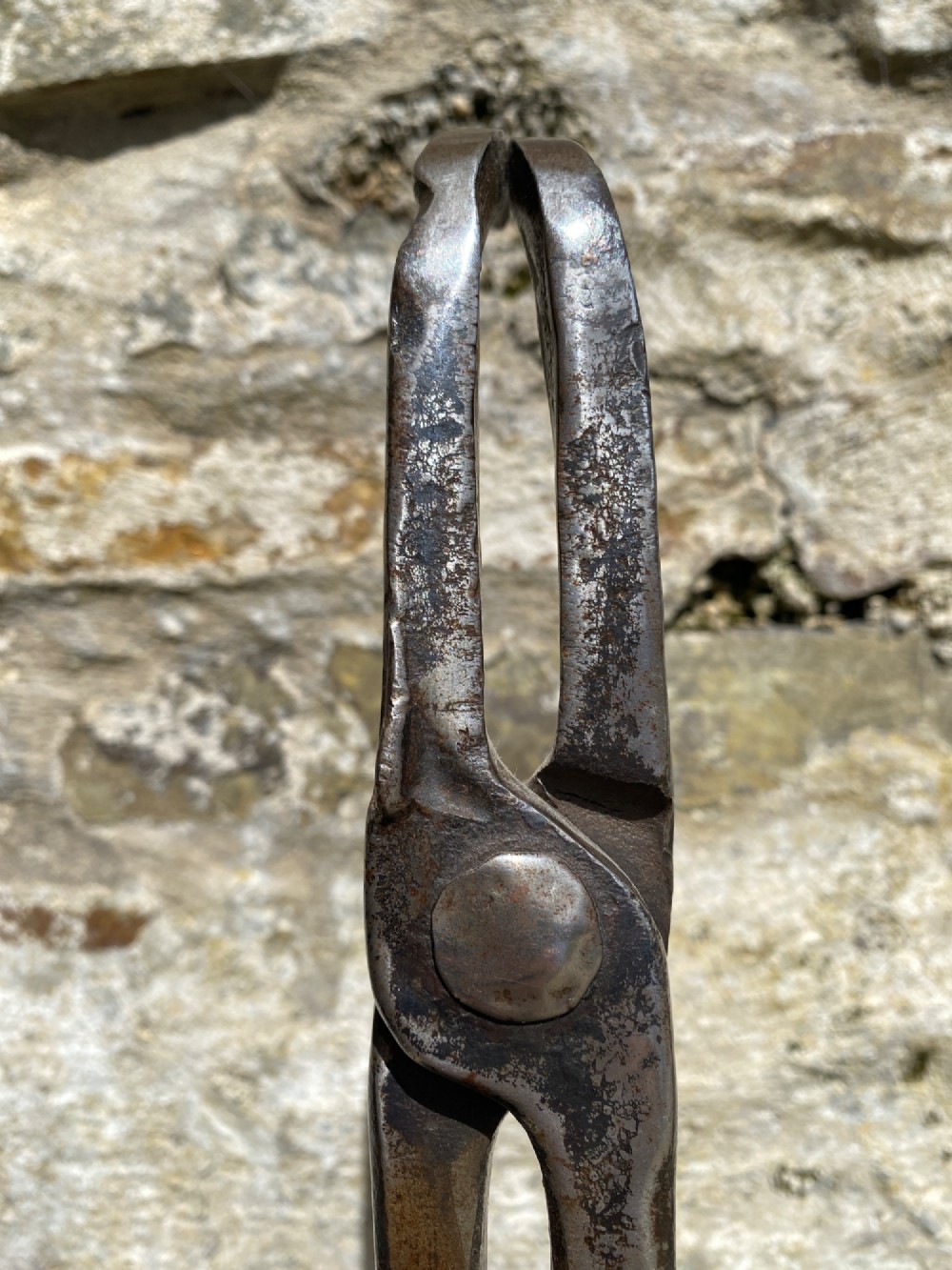 A forged steel tool with an integral lower hook mounted vertically into a square dark wooden block engraved with a cross and text. View X