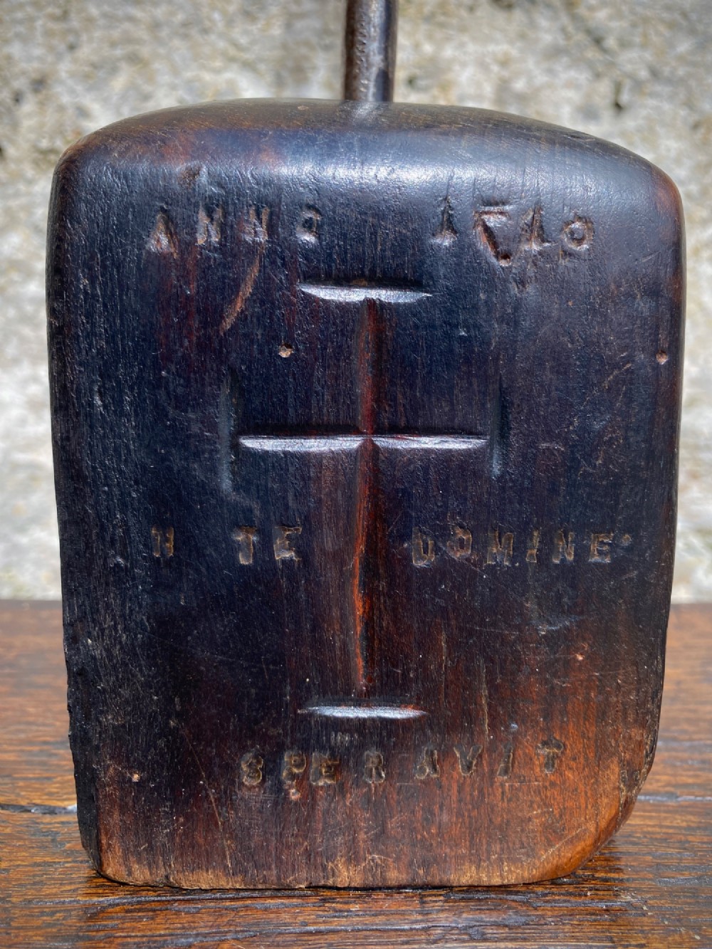 A forged steel tool with an integral lower hook mounted vertically into a square dark wooden block engraved with a cross and text. View XII