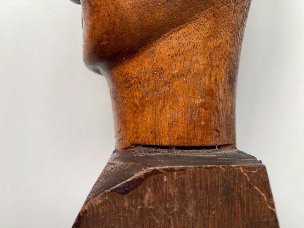 A small hand-carved wooden head sculpture on a square base with stylized eyes and mouth in a warm brown finish. View IV