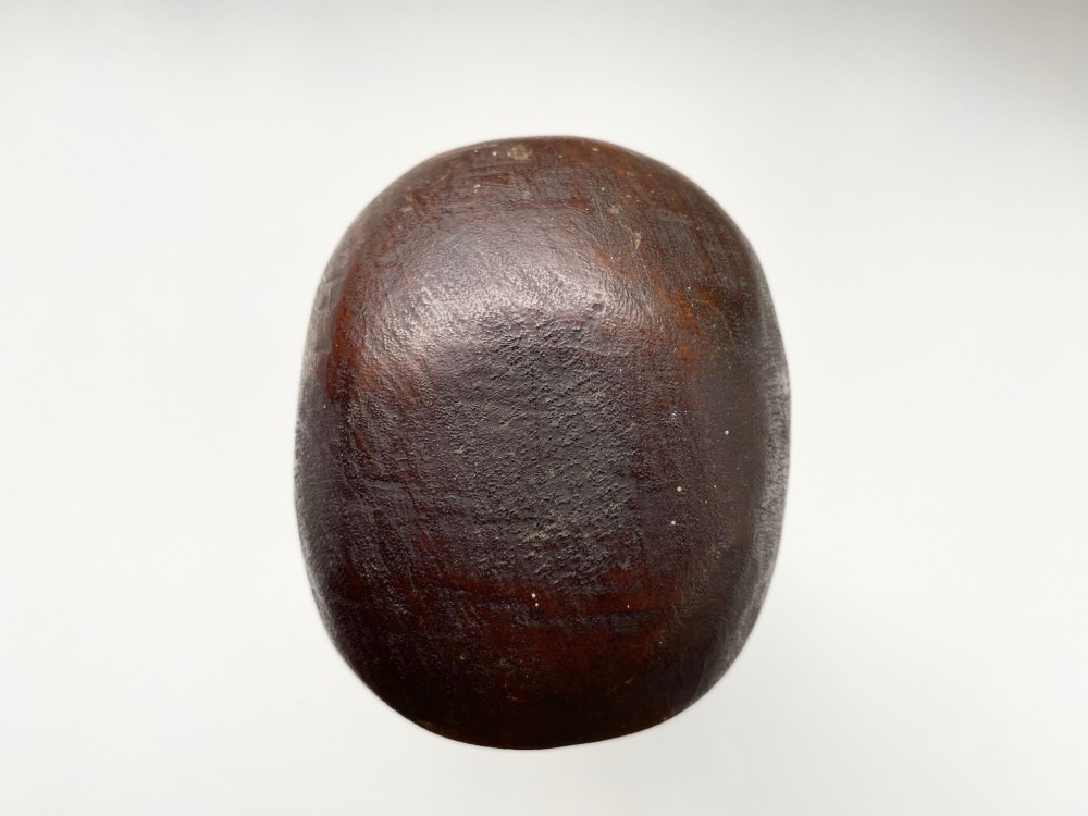 A small hand-carved wooden head sculpture on a square base with stylized eyes and mouth in a warm brown finish. View VIII
