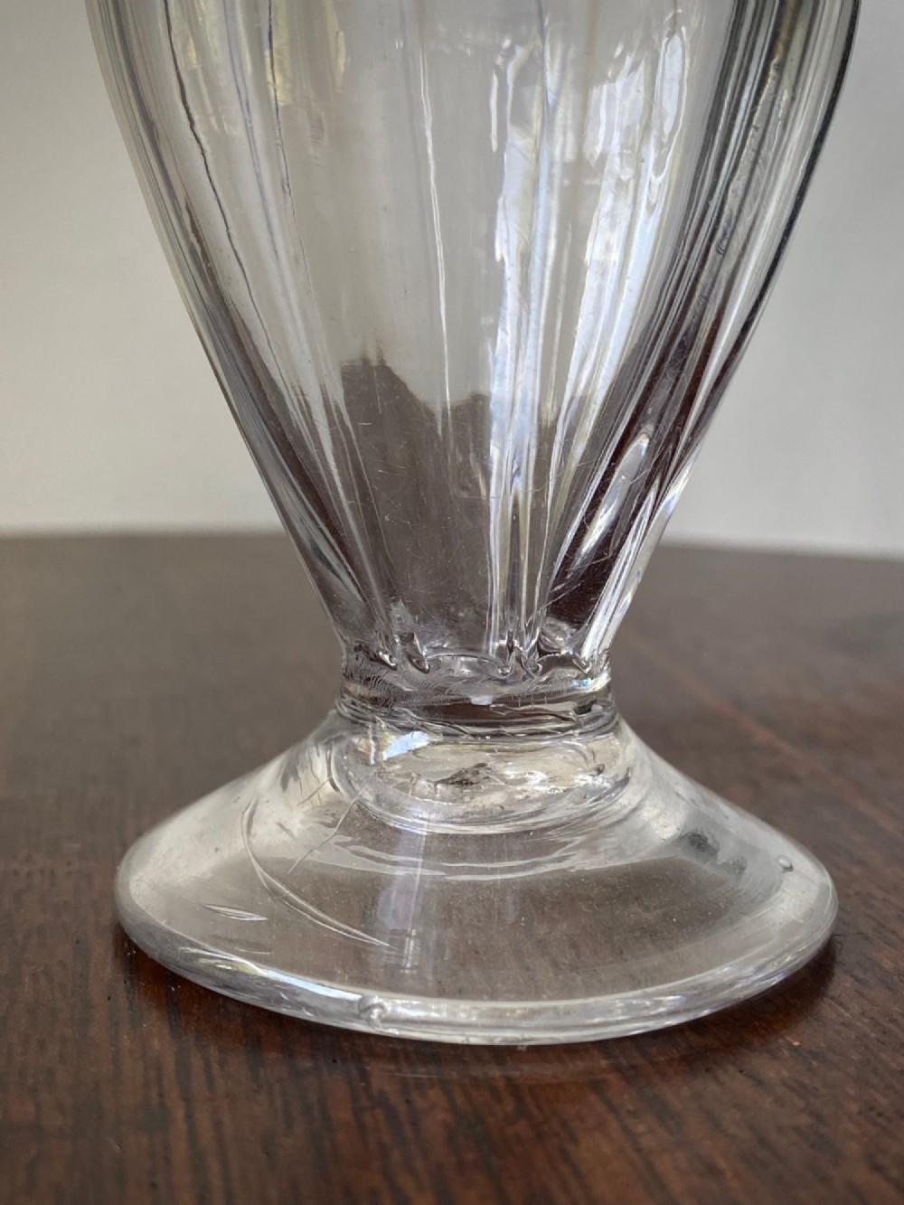 An 18th-century clear hand-blown glass dry mustard jar featuring vertical fluting, a circular footed base, and a removable pointed glass stopper. View IV