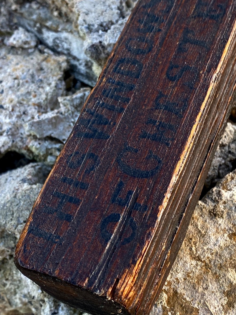 A square-cut dark oak table leg featuring hand-carved lettering along its shaft and a brass collar at the tapered base. View III