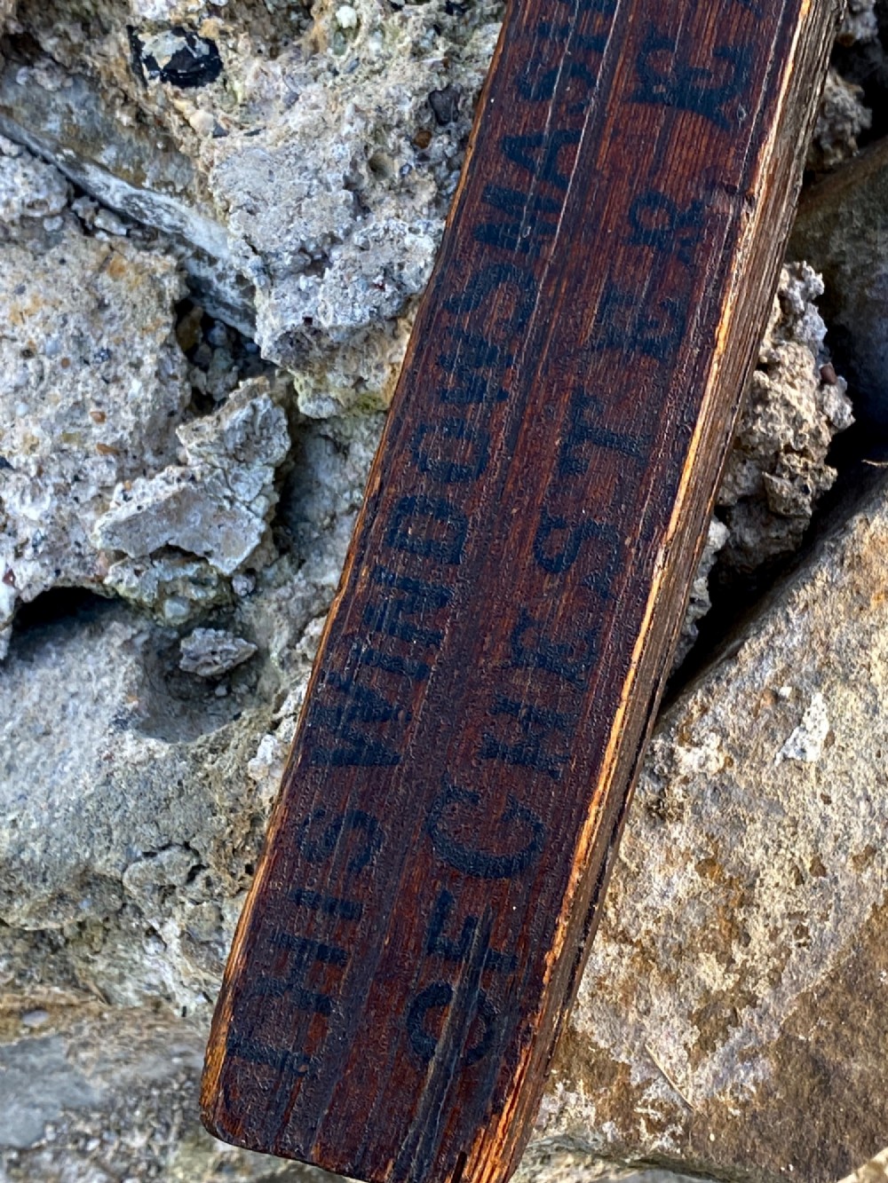 A square-cut dark oak table leg featuring hand-carved lettering along its shaft and a brass collar at the tapered base. View IV