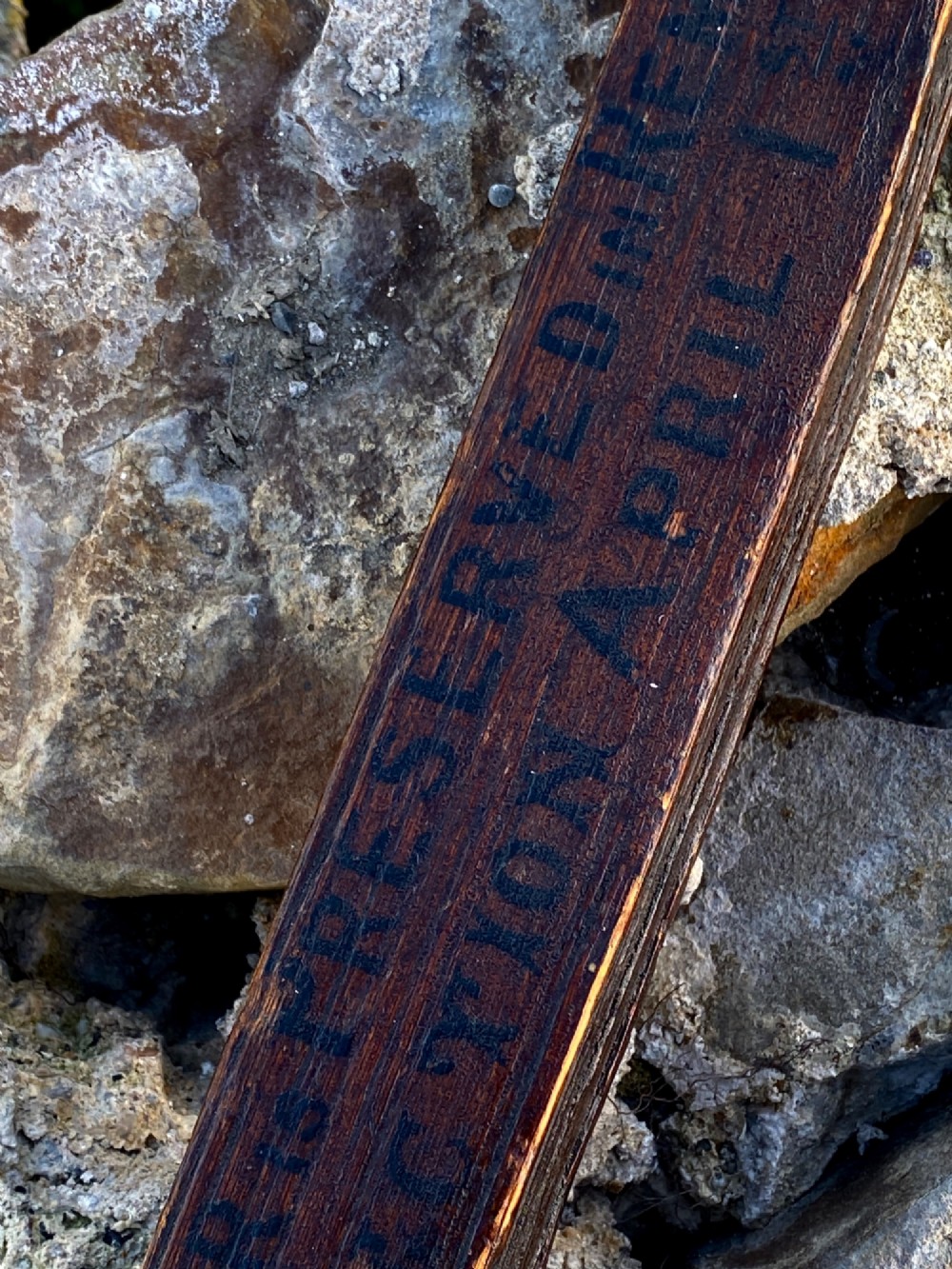 A square-cut dark oak table leg featuring hand-carved lettering along its shaft and a brass collar at the tapered base. View V