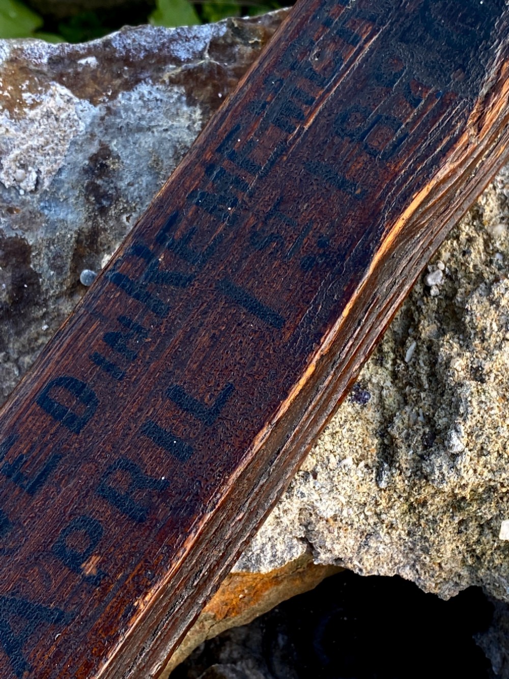 A square-cut dark oak table leg featuring hand-carved lettering along its shaft and a brass collar at the tapered base. View VI