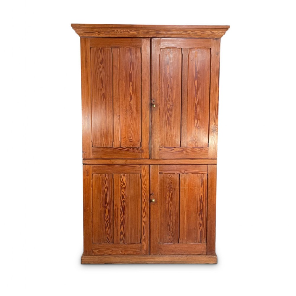 A tall two-tier antique pitch pine chapel cupboard featuring four fielded panel doors and a moulded top cornice.