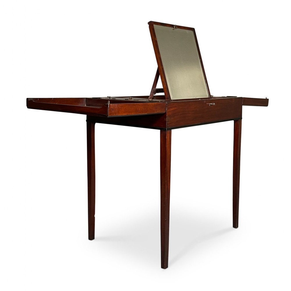 An antique dark mahogany dressing table featuring an open central pop-up mirror, two extended side leaves, and slim square tapered legs.