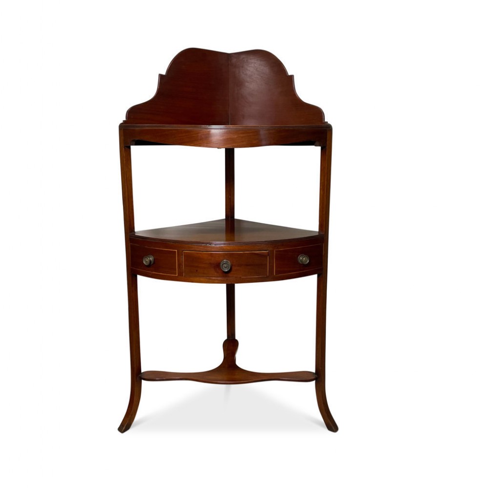 A George III mahogany corner washstand featuring a shaped upstand backboard, a curved tier with a central drawer, turned brass knobs, slender splayed legs, and a curved lower stretcher.
