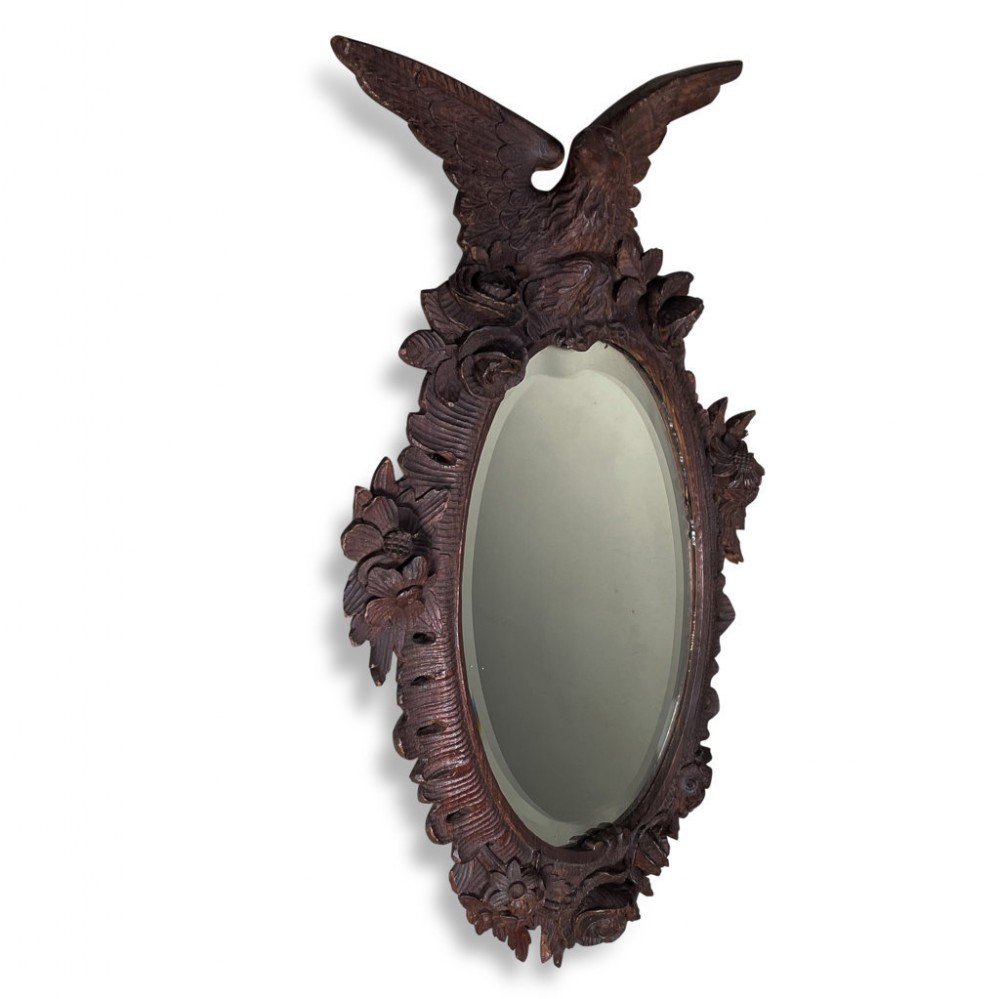 An oval wall mirror framed in dark hand-carved wood featuring a crested eagle with outstretched wings and carved floral embellishments.