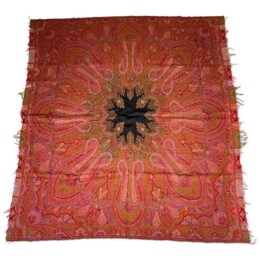 A square antique woollen shawl decorated with dense red, orange, and green paisley motifs and a black central star medallion.