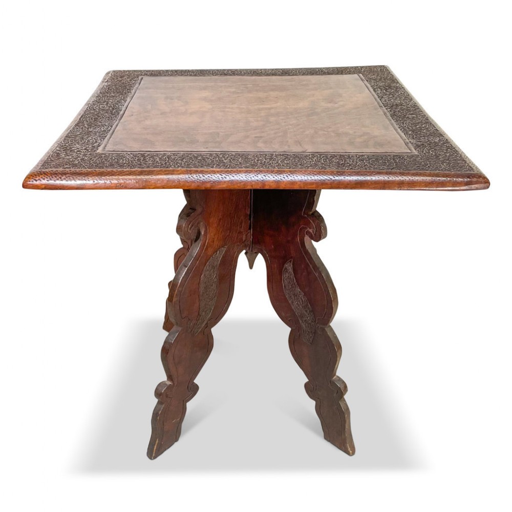 A square dark hardwood side table featuring a carved floral border around a smooth top panel and four shaped carved legs.