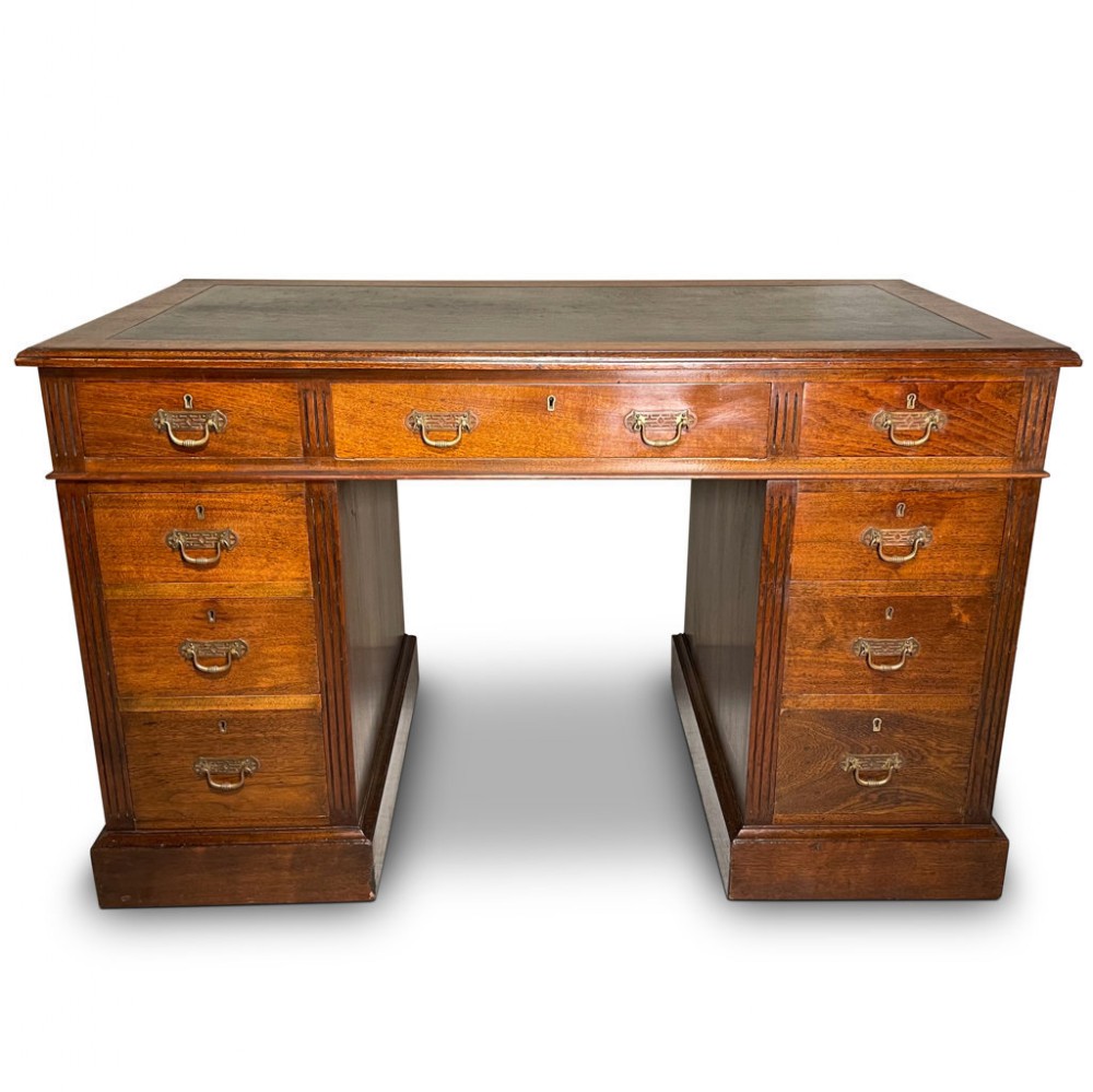 A warm brown oak twin pedestal desk featuring a leather inset writing surface, nine drawers, and brass handles.