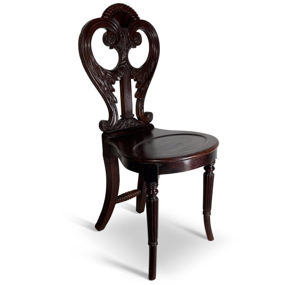 A dark mahogany Regency hall chair featuring an open carved back with scroll motifs, a solid wooden seat, and fluted turned front legs.