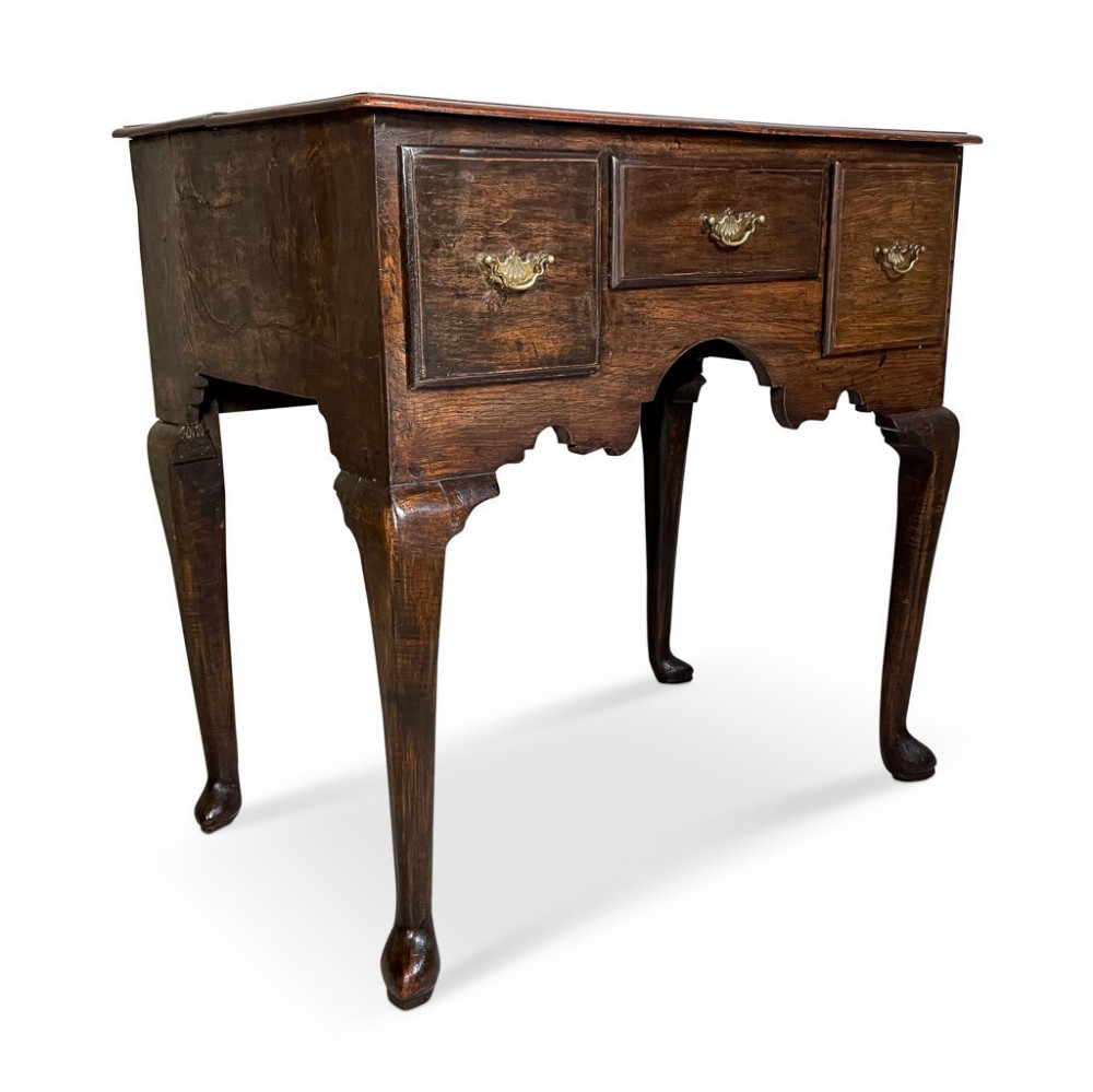 An antique dark oak lowboy featuring three frieze drawers with brass handles, a shaped apron, and cabriole legs ending in pad feet.
