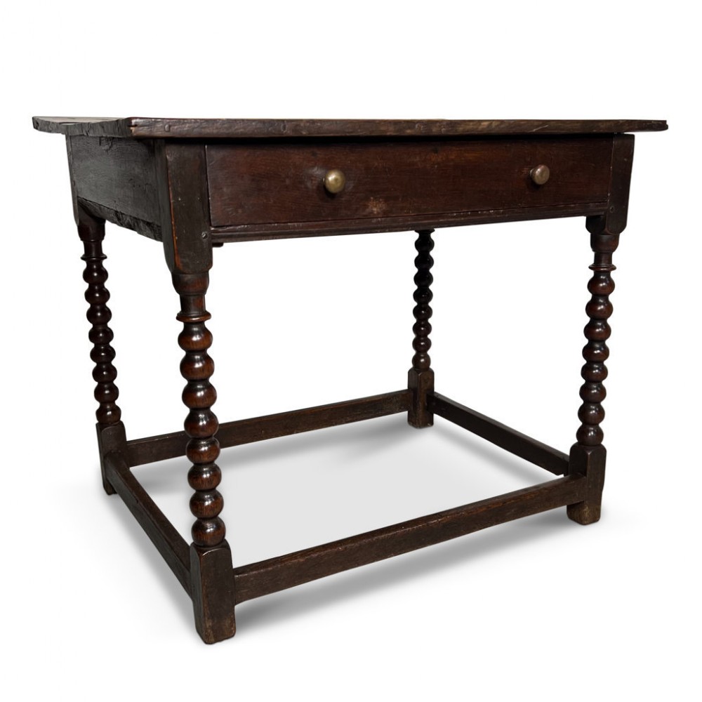 A dark oak jointed side table featuring bobbin-turned legs, a single frieze drawer with brass knobs, and perimeter stretchers.