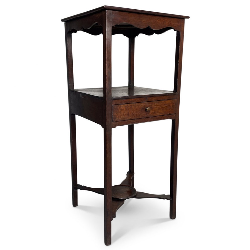 A tall dark oak nightstand featuring an open upper shelf with a scalloped apron, a middle shelf incorporating a single drawer, straight legs, and an X-shaped stretcher base.