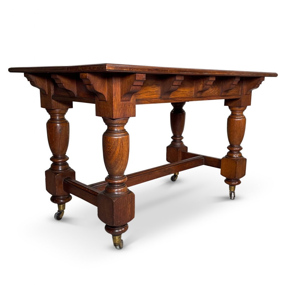 A Victorian dark oak centre table with heavy baluster turned legs, a rectangular top, bracketed apron, low stretcher, and brass castors.