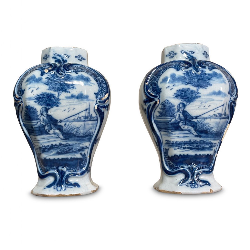 A pair of baluster-shaped blue and white Delftware vases featuring hand-painted pastoral scenes framed by raised rococo scrollwork.