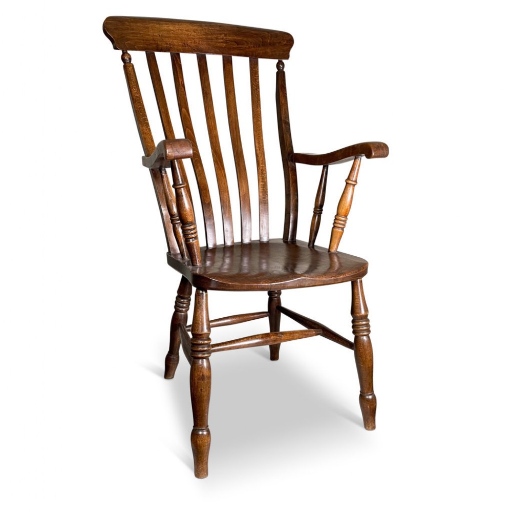 A warm brown wooden elbow chair featuring a high splat and spindle backrest, curved arms on turned supports, a contoured solid seat, and turned legs linked by stretchers.