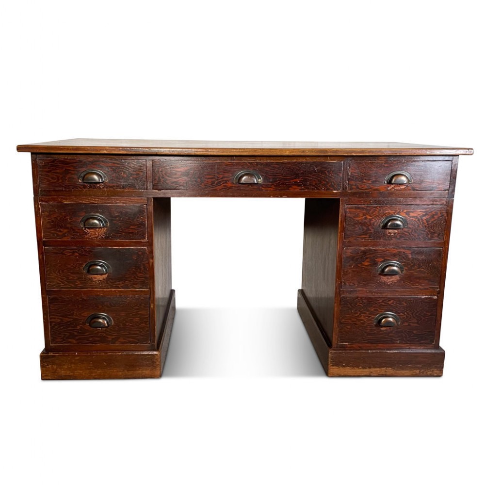 A dark stained pine pedestal desk featuring nine drawers fitted with metallic cup handles and a central kneehole.