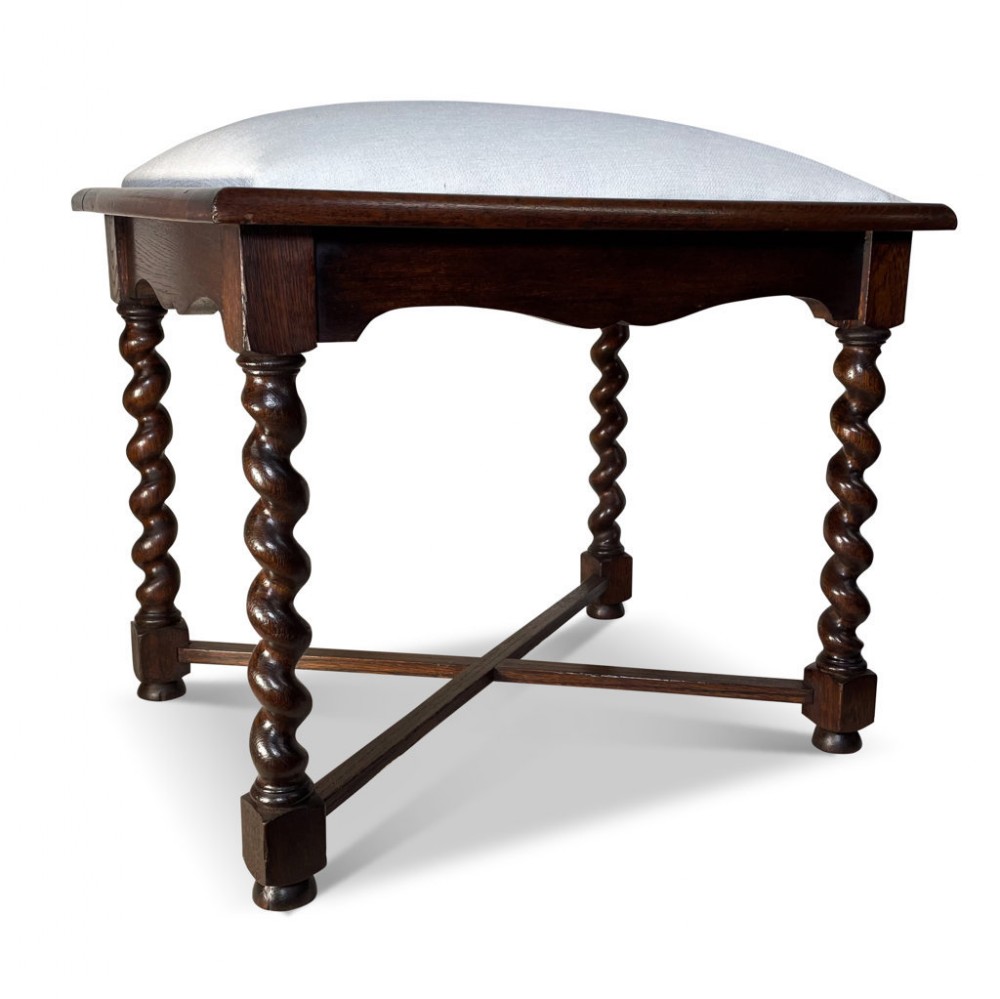 A dark oak stool featuring four spiralled barley twist legs connected by a central X-frame stretcher and topped with a light greyish-blue upholstered seat.