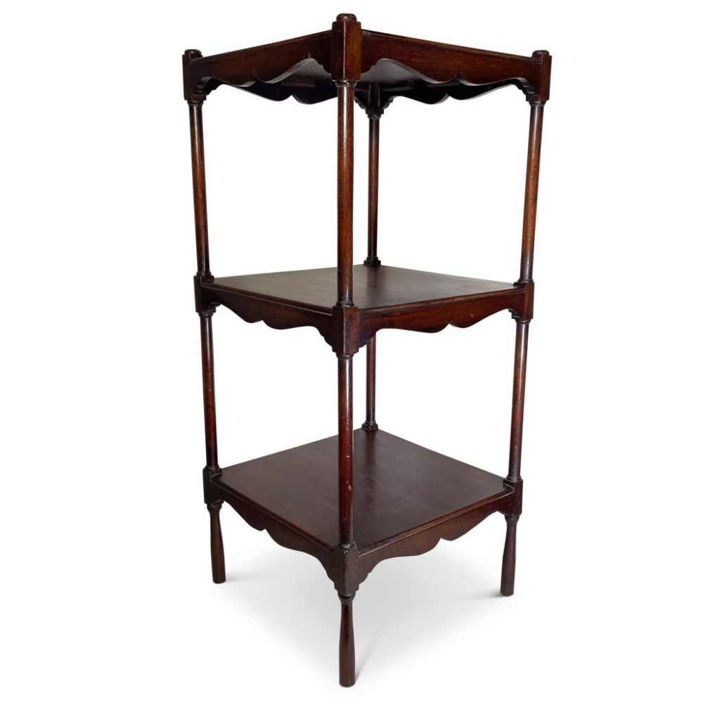 A Victorian mahogany three-tiered whatnot featuring turned vertical columns, scalloped aprons under each square shelf, and simple turned feet.