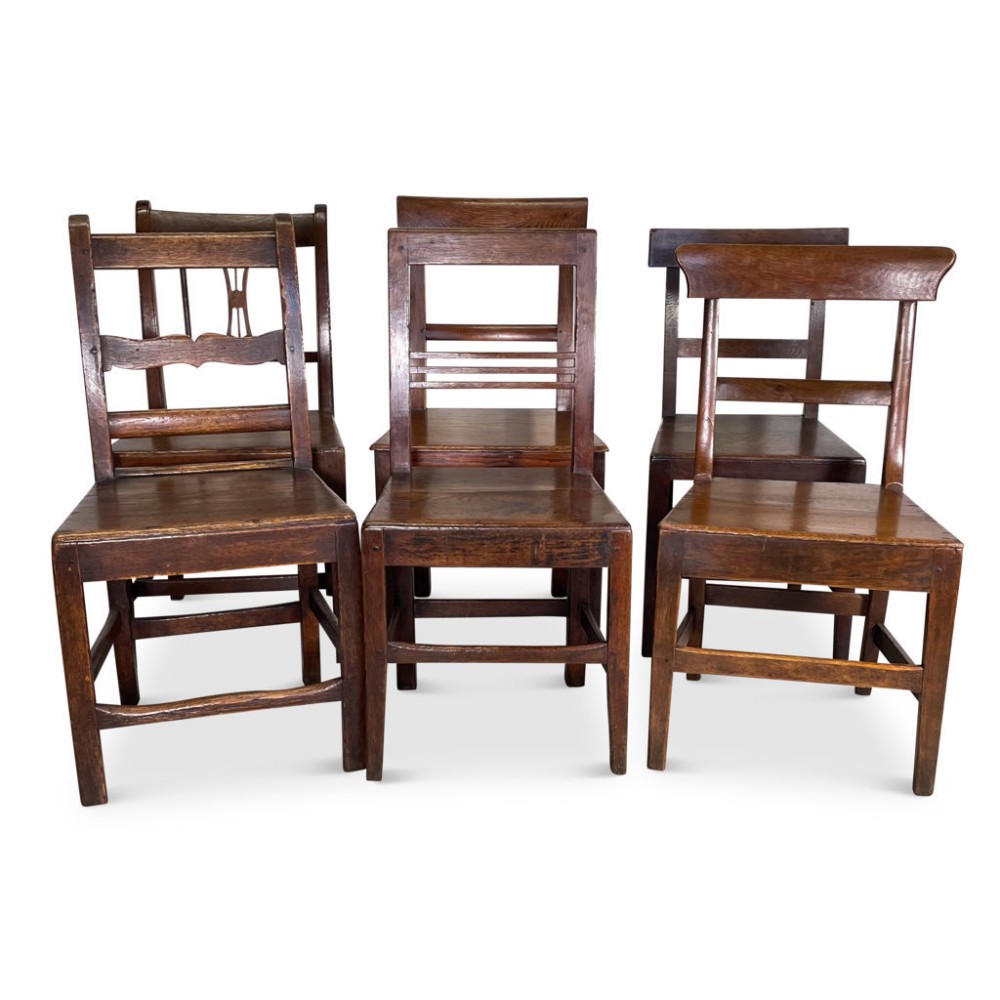 A set of six dark brown George III oak and elm dining chairs featuring timber seats and varied horizontal back rails.