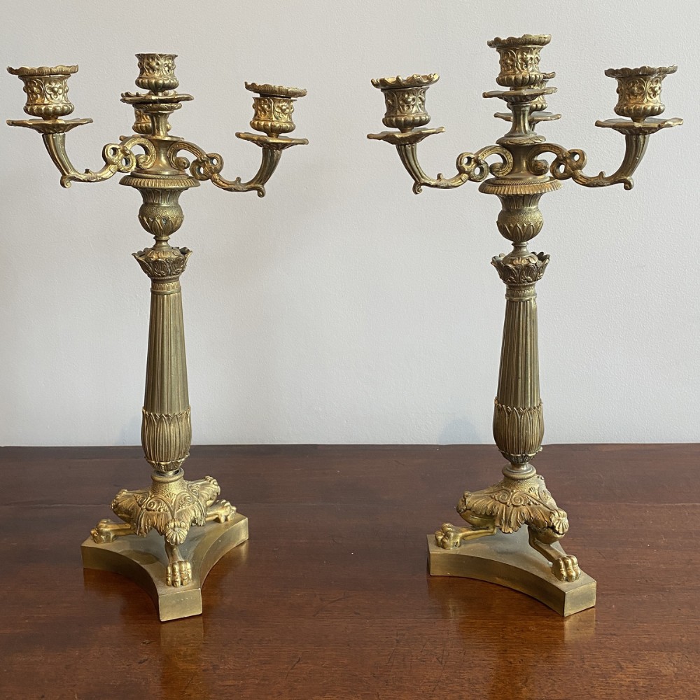 A pair of ornate French gilt brass three-arm candelabra featuring fluted central columns and claw-foot triangular bases.