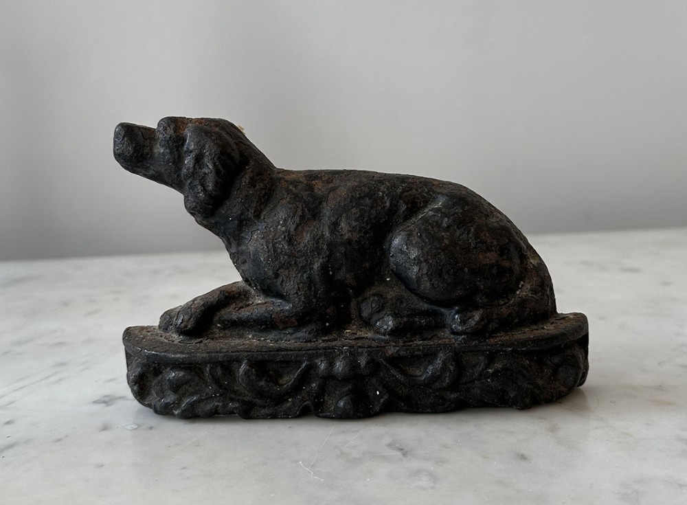 A dark Victorian cast iron doorstop formed in the shape of a reclining dog seated on an ornate plinth base.