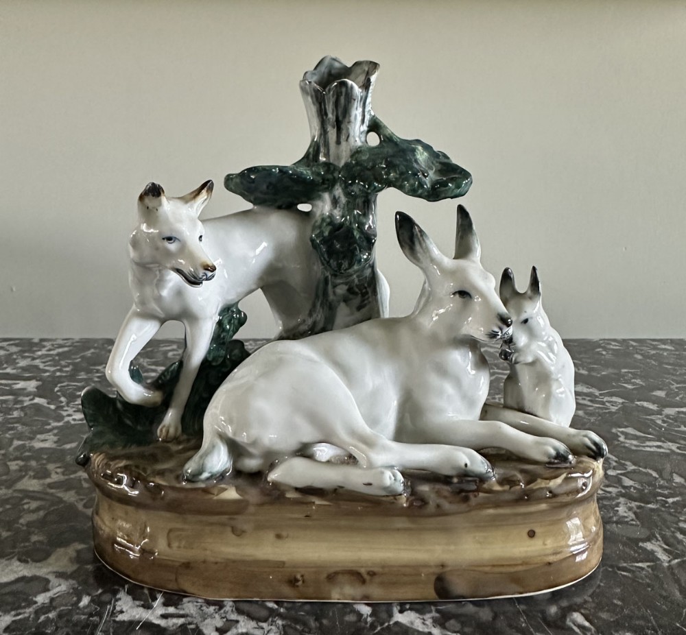 A glazed ceramic figure group depicting a white fox standing beside a tree trunk column and a white hare resting with a leveret on a naturalistic base.