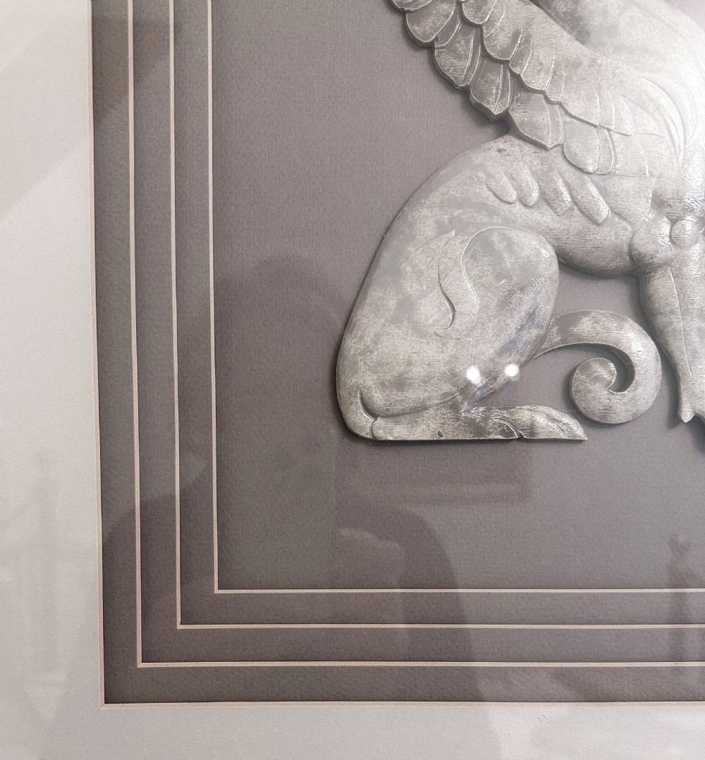 A pair of framed relief sculptures depicting carved stone griffin figures facing each other within layered grey mounts and gold frames. View V