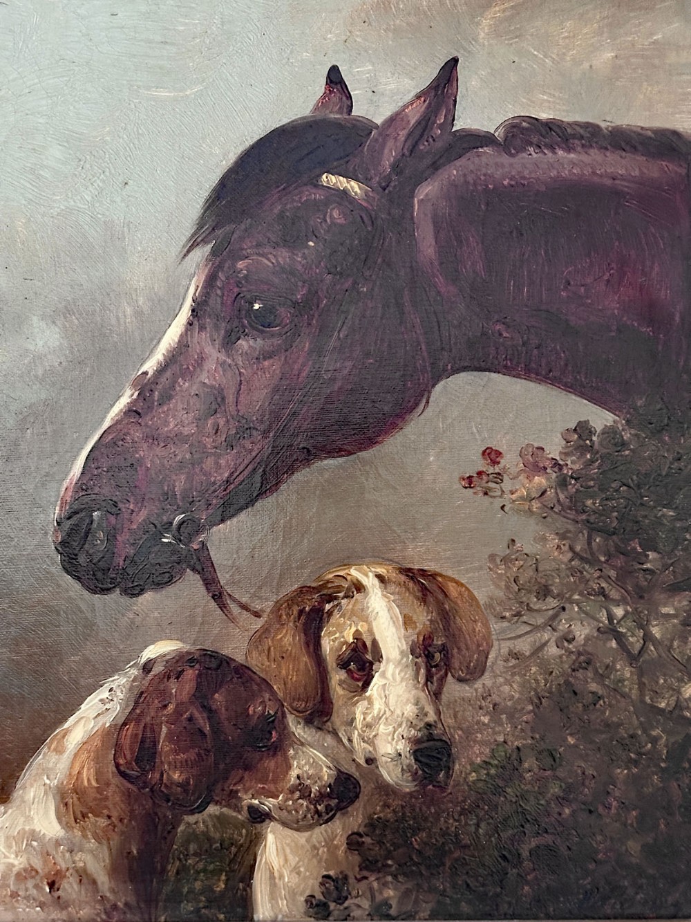 An antique oil painting depicting the profile of a dark horse looking down at two brown and white hunting hounds against a muted background.