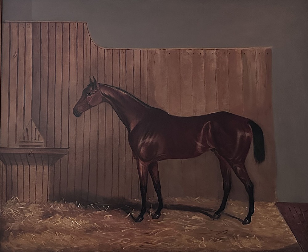 An oil painting depicting a bay racehorse standing in profile inside a wooden stable stall lined with straw.