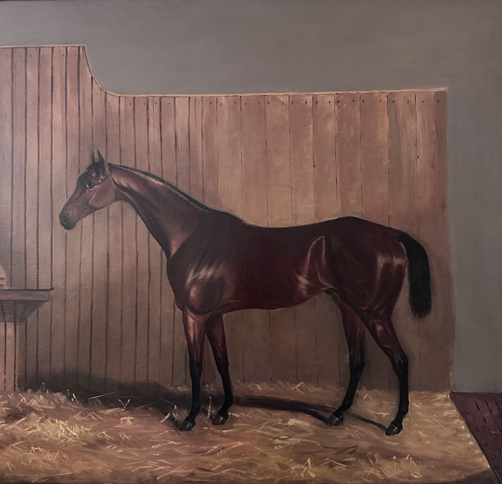 An oil painting depicting a bay racehorse standing in profile inside a wooden stable stall lined with straw. View III