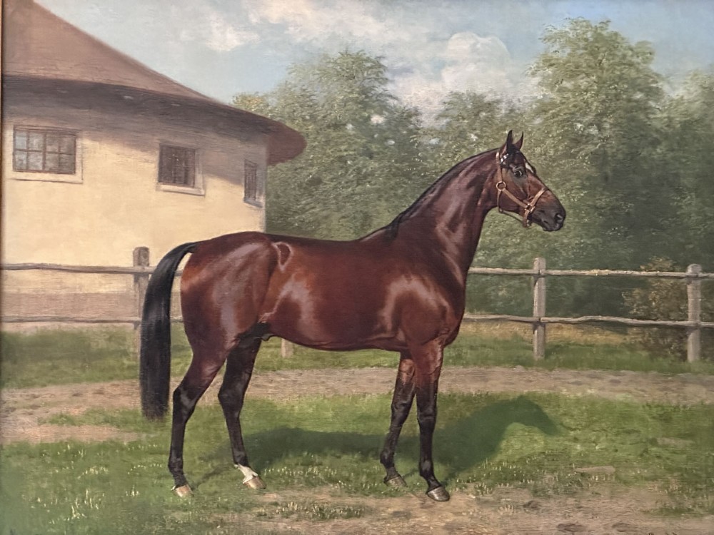 An antique oil painting depicting a bay horse standing in profile wearing a leather bridle in an outdoor paddock in front of a circular building.