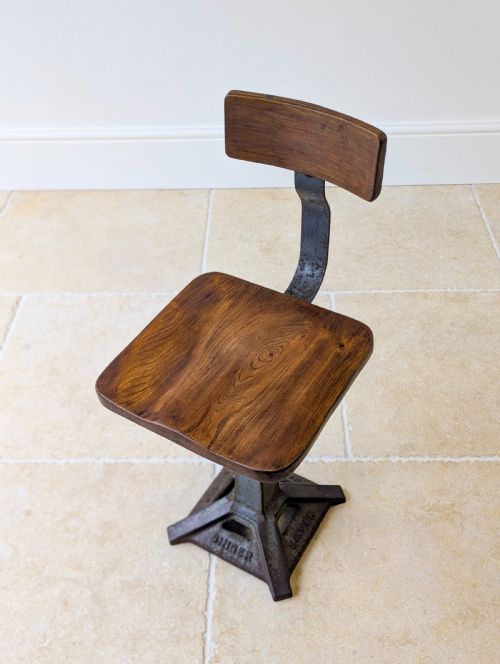 fig 1. An early 20th-century Singer industrial chair featuring a dark cast iron pedestal base, a threaded height-adjustment mechanism, and a shaped elm seat with an attached wooden backrest.