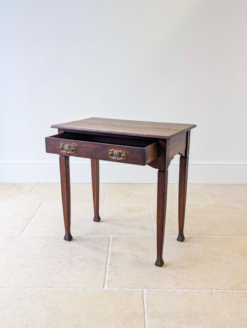 fig 1. An antique dark oak side table featuring a single drawer with brass drop handles, shaped corner aprons, and slender tapered legs.