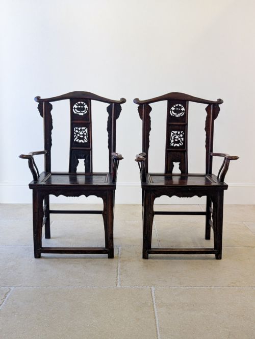 fig 1. A pair of dark brown carved wooden Chinese yoke-back armchairs with curved top rails, open arms, and carved back splats.