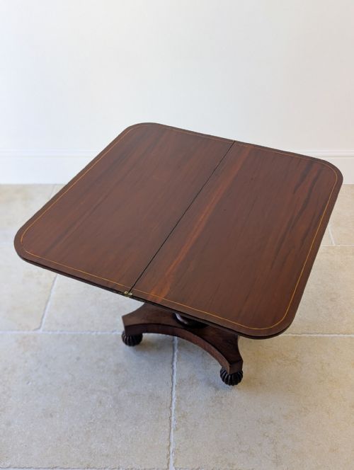 fig 1. An antique William IV dark mahogany fold-over tea table featuring a carved central pedestal column, quadform platform base, and lobed feet.