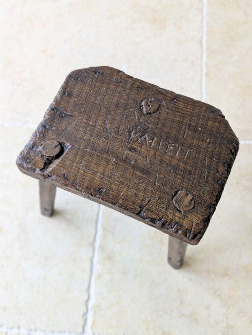 fig 1. A dark oak Victorian three-legged stool featuring a thick rectangular top and weathered splayed legs.