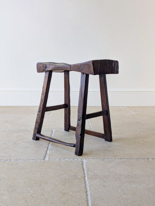 fig 1. A dark oak 18th-century stool featuring a concave dished seat, splayed legs, and rustic wooden stretchers.
