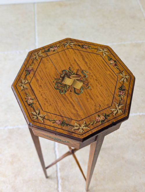 fig 1. An Edwardian octagonal satinwood candle stand featuring painted floral borders, four slender tapered legs, and an X-form stretcher with a central finial.