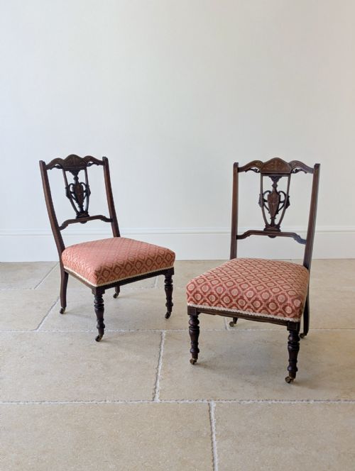 fig 1. A pair of Edwardian mahogany salon chairs featuring urn marquetry splats, turned front legs on brass castors, and patterned upholstery.