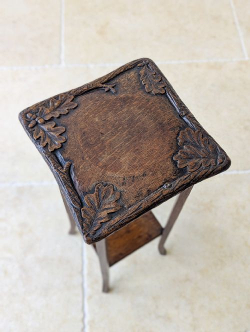 fig 1. A tall Edwardian Arts and Crafts oak plant stand featuring a carved square top surface, a lower tier shelf, and four slender gently splayed legs.
