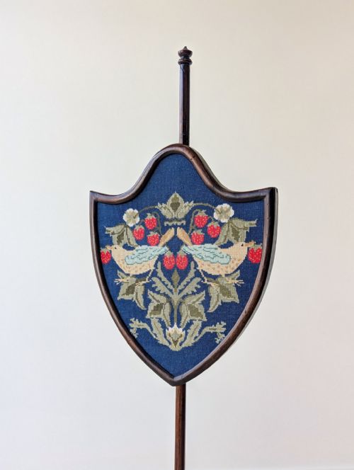 fig 1. An antique George III mahogany pole screen featuring a tripod base, turned column, and a shield-shaped needlework panel depicting birds and strawberries.